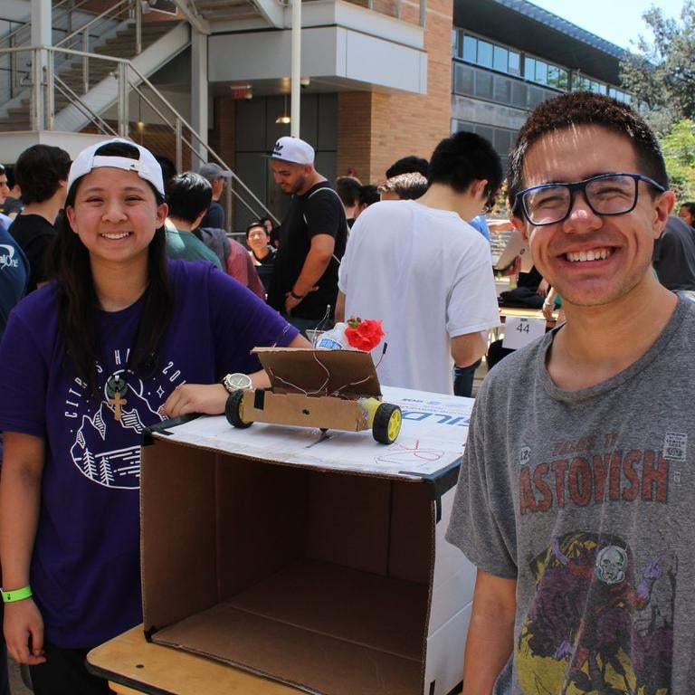 two people smiling in a crowd next to their display of an engineering project